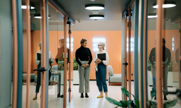 Two colleagues walking and having a discussion in an office hallway.